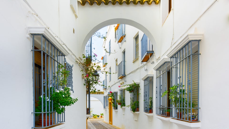 A narrow alley in Almeria, Andalusia, Spain, with white buildings, arched passages, and decorative windows with potted plants.