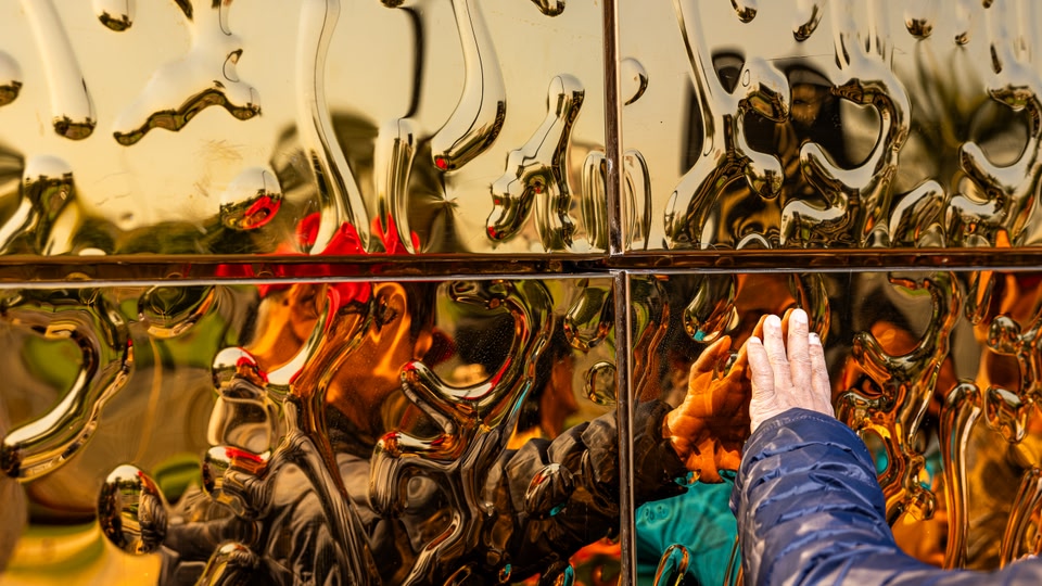 A person touching a golden reflective wall, which is part of the Dubai Frame in Dubai, United Arab Emirates.