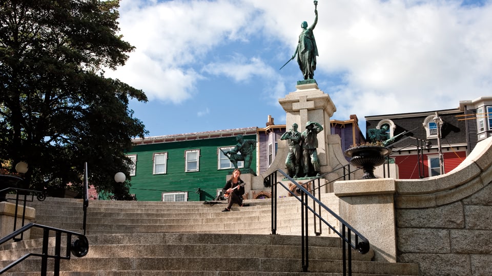 A woman sits on steps playing a guitar in front of a monument depicting historical figures.