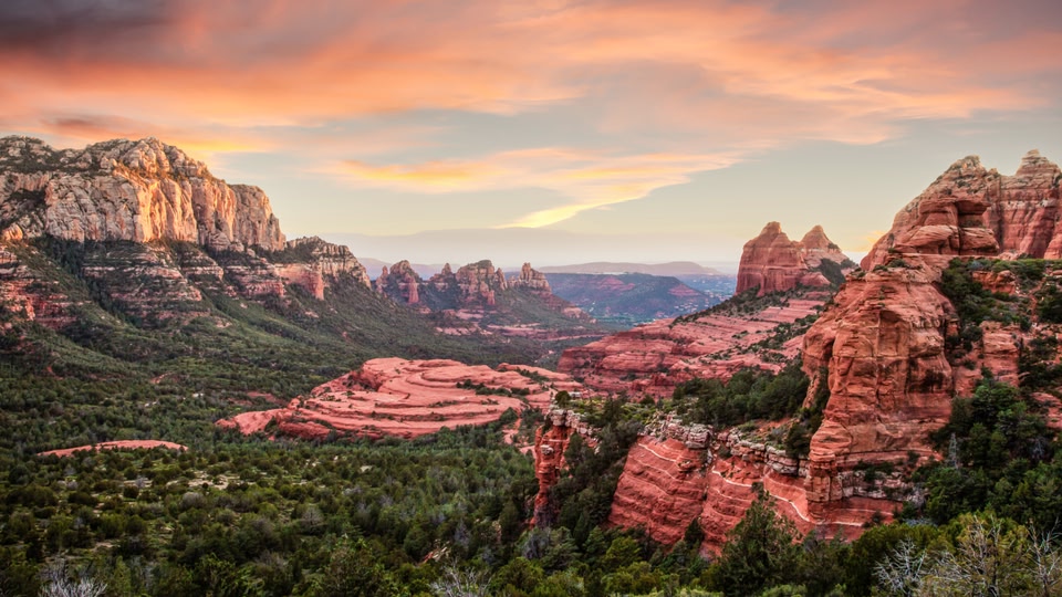 A scenic view of red rock formations and lush greenery under a vibrant sunset sky.