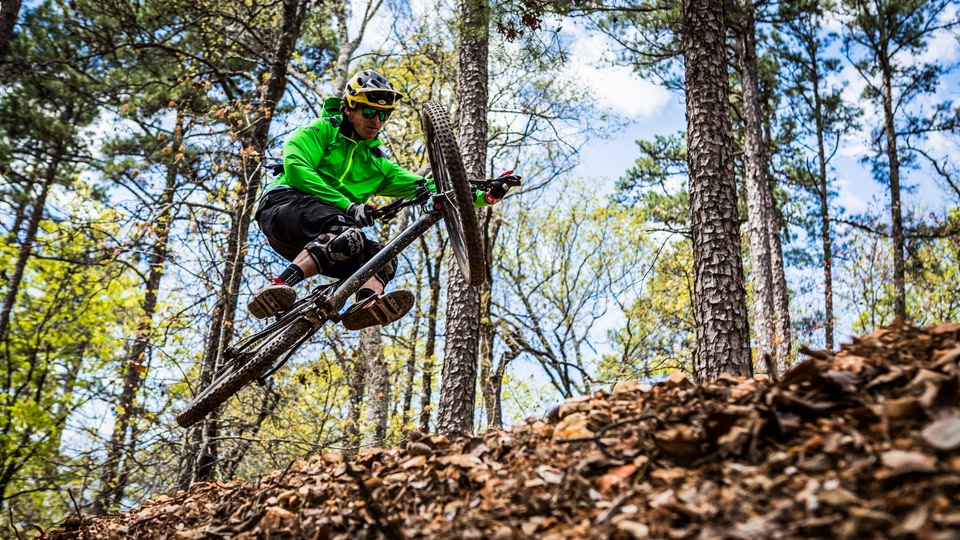 A person in a green jacket and helmet rides a mountain bike through a forest.