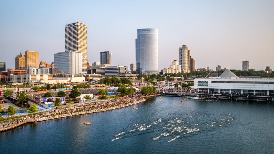 Aerial view of a cityscape with a large group of swimmers participating in an event in the foreground.