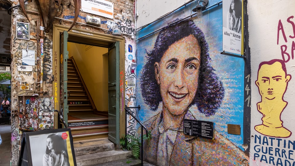 Facade of the Anne Frank Zentrum in Berlin with a mural of Anne Frank and various signs and posters.