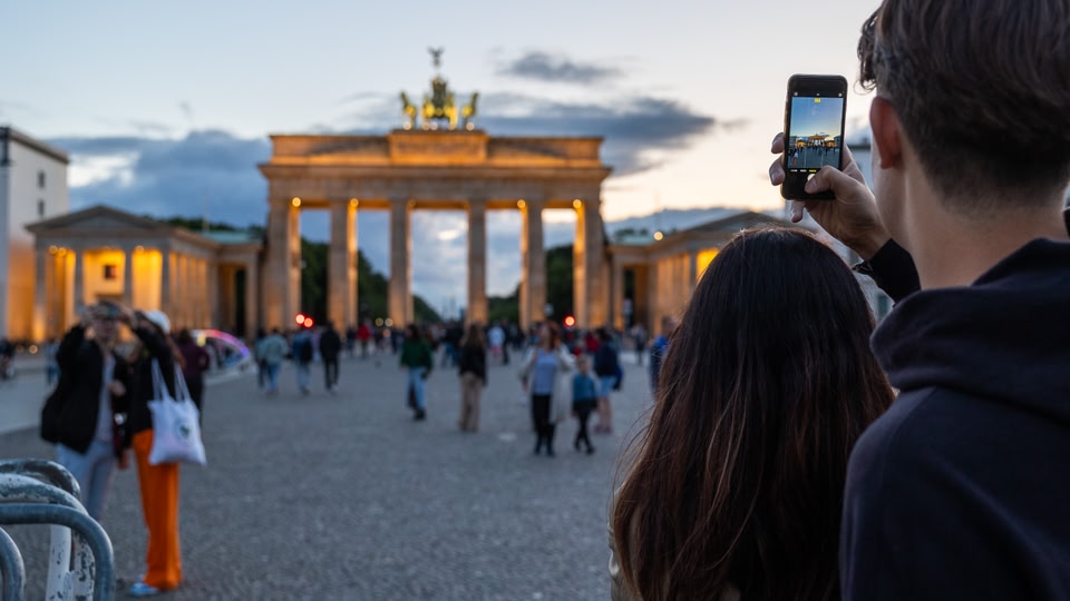 A man and a woman taking a photo of the Brandenburg Gate at sunset.