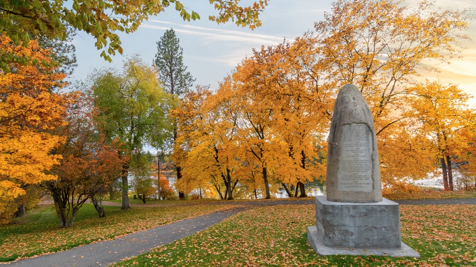 A stone monument in a park with autumn-colored trees and a pathway.