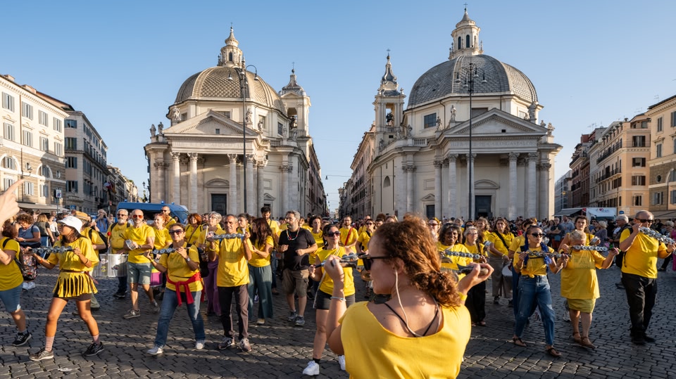 A group of people dressed in yellow shirts play instruments in a public square surrounded by historic buildings.