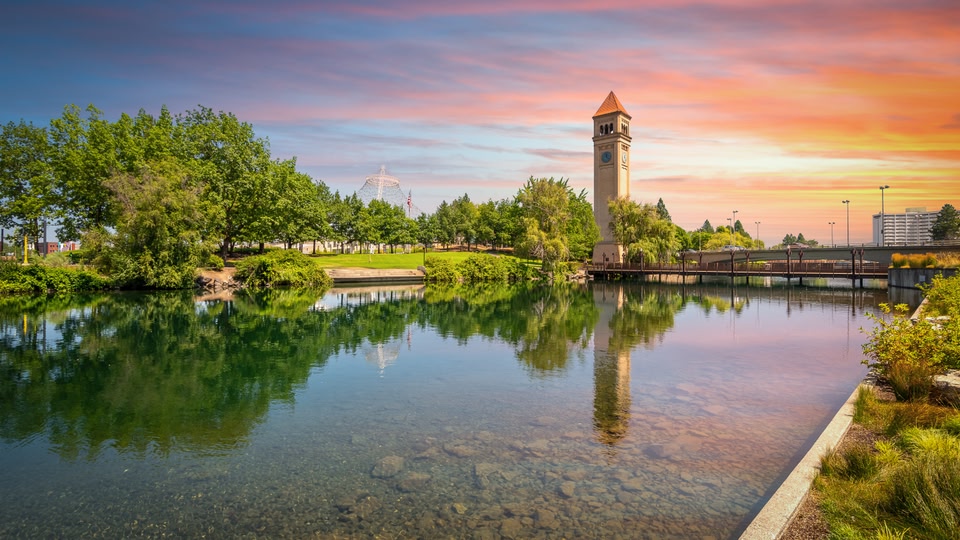 A serene scene at sunset with a historic clock tower in the background, standing by a calm river in Spokane, Washington.