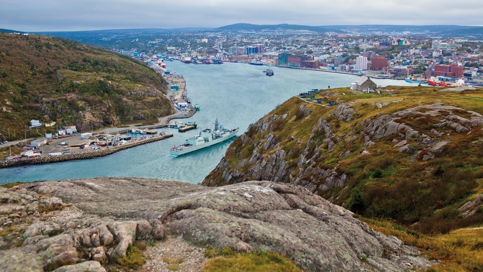Aerial view of St. John's, Newfoundland and Labrador, Canada, showcasing the city skyline, harbor with ships, and surrounding landscape.