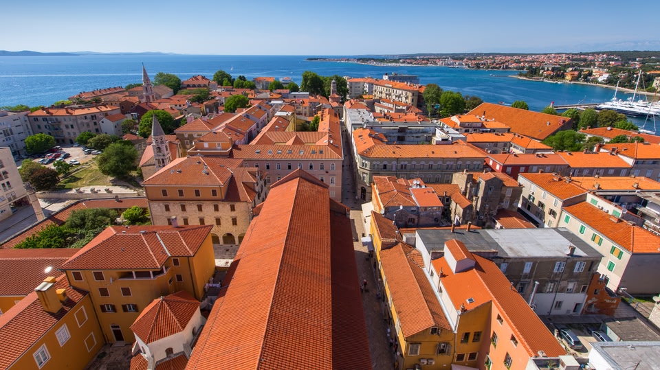 Aerial view of Zadar, Croatia, showcasing the cityscape with orange rooftops, waterfront, and the sea in the background.