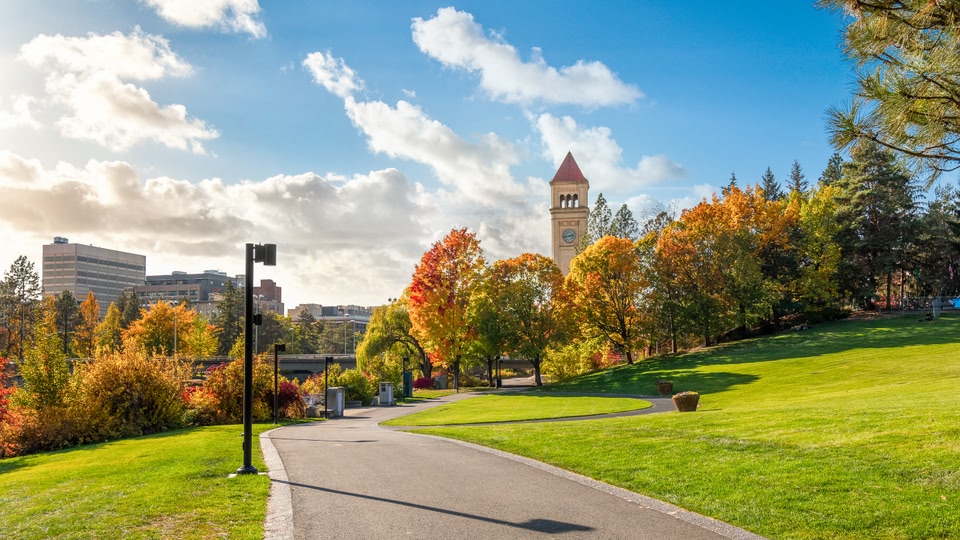 A scenic park pathway with colorful autumn trees and a clock tower in the background, illuminated by bright sunlight.