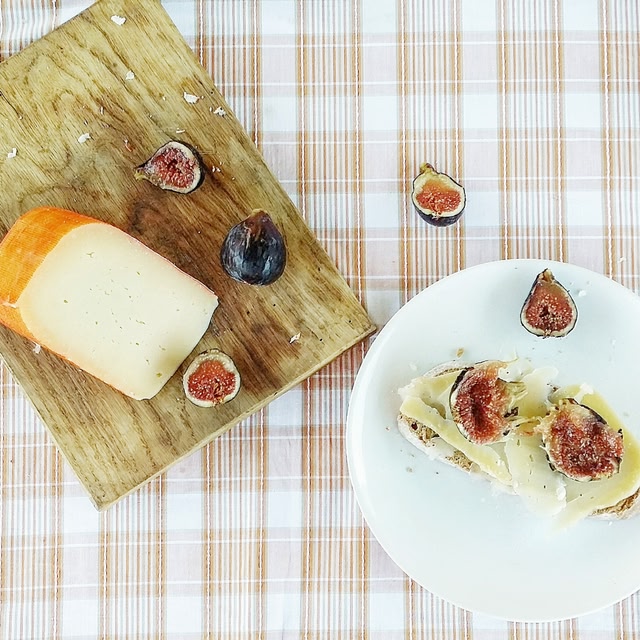 A plate with sliced figs and cheese on a wooden cutting board placed on a plaid tablecloth.
