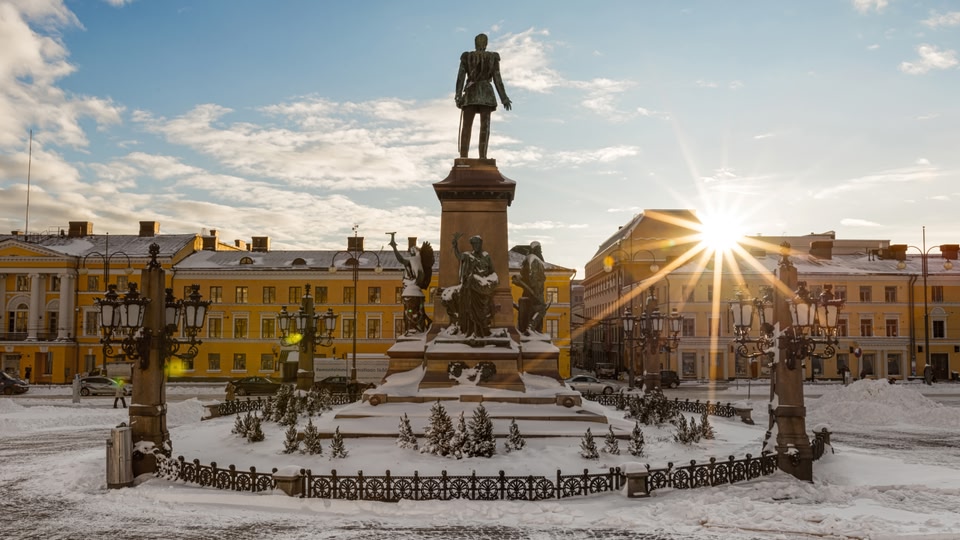 A statue in a snowy urban square at sunrise with bright sunlight and clear blue skies.