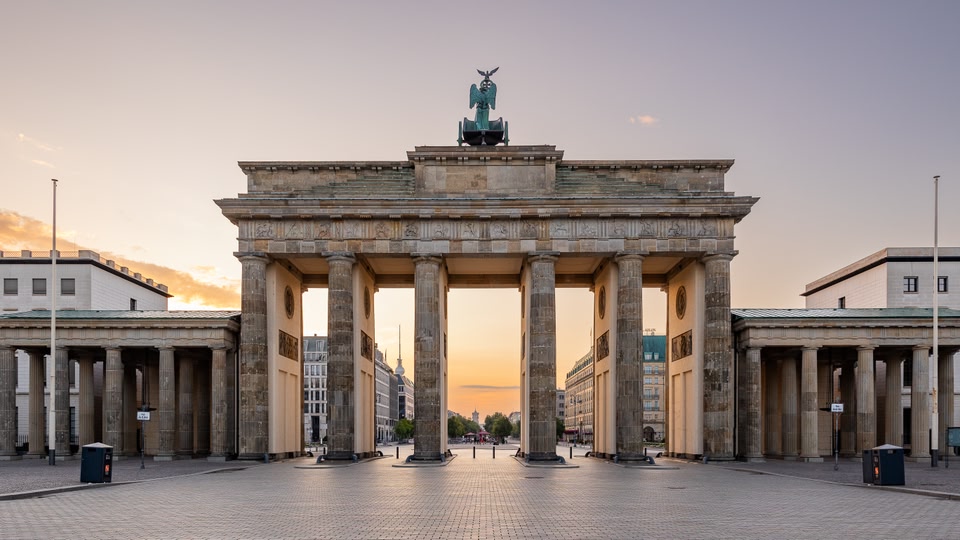 Brandenburg Gate in Berlin, Germany, captured at sunrise or sunset, showing the historic and iconic structure with warm lighting.