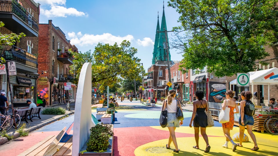 A vibrant urban street scene in Montreal with colorful buildings, pedestrians, and a community gathering area.