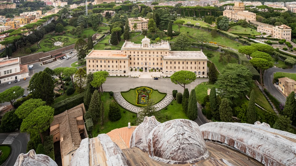 Aerial view of St. Peter's Basilica in Rome surrounded by gardens and other historic buildings.