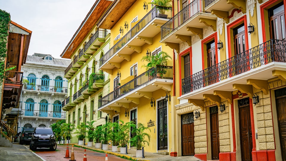 Bright colonial facades with wrought-iron balconies and potted palms on a Panama City street.