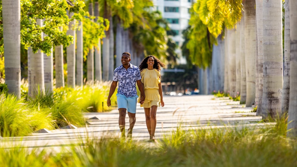 A couple walking hand in hand down a tree-lined path in Miami, Florida.