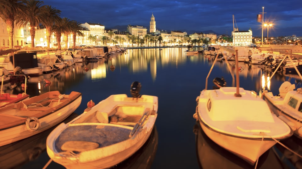 Boats docked at a waterfront at night with city lights reflecting on the water