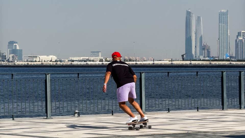 A person skateboarding along a waterfront promenade with a city skyline in the background.