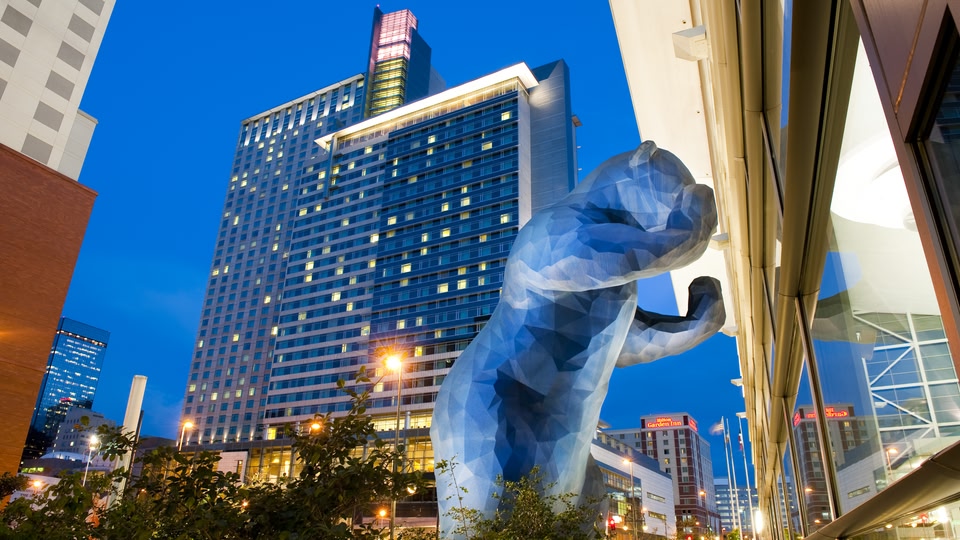A large, illuminated bear statue in a city square at night, with modern buildings in the background.