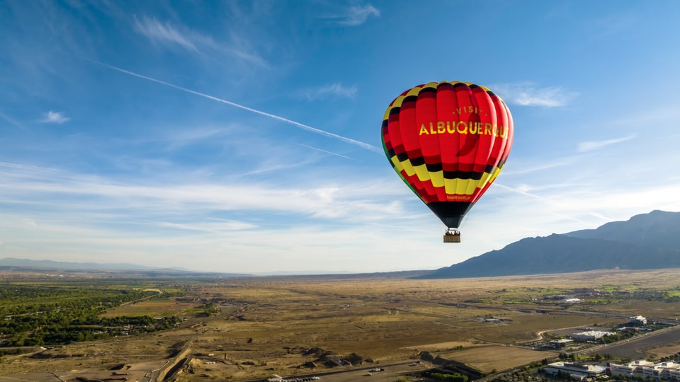 A hot air balloon with the text 'VISIT ALBUQUERQUE' floating in the sky above a desert landscape.