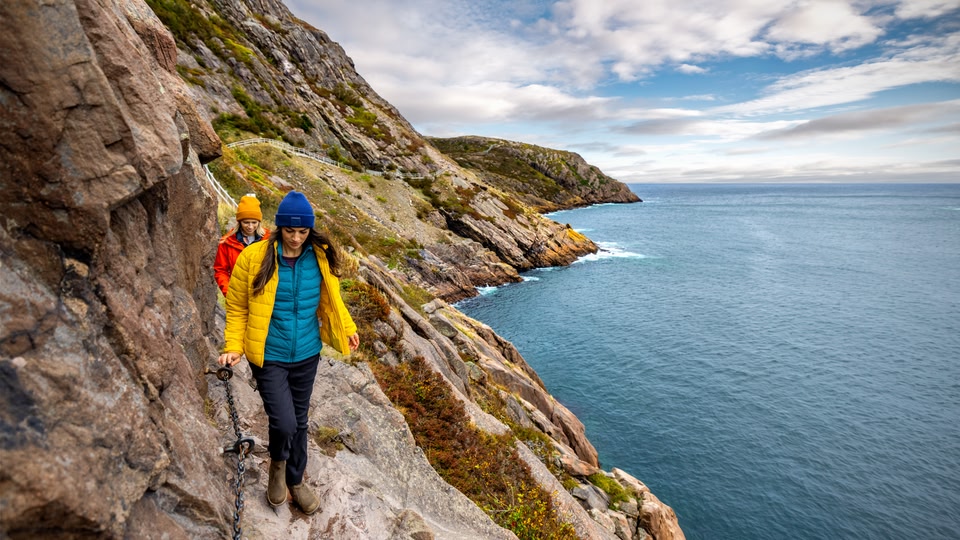 Two people hiking along a rocky coastal trail with the ocean in the background.