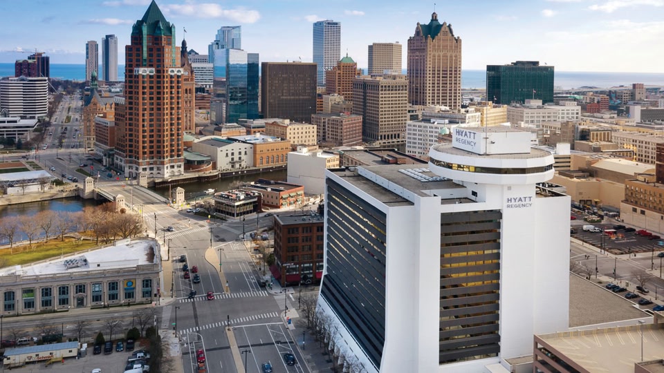 Aerial view of Milwaukee skyline showing modern and historic buildings, with a prominent Hyatt Regency hotel in the foreground.