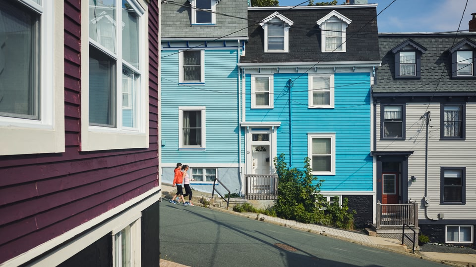 Two people walking on a street lined with brightly colored houses in Saint John, New Brunswick, Canada.