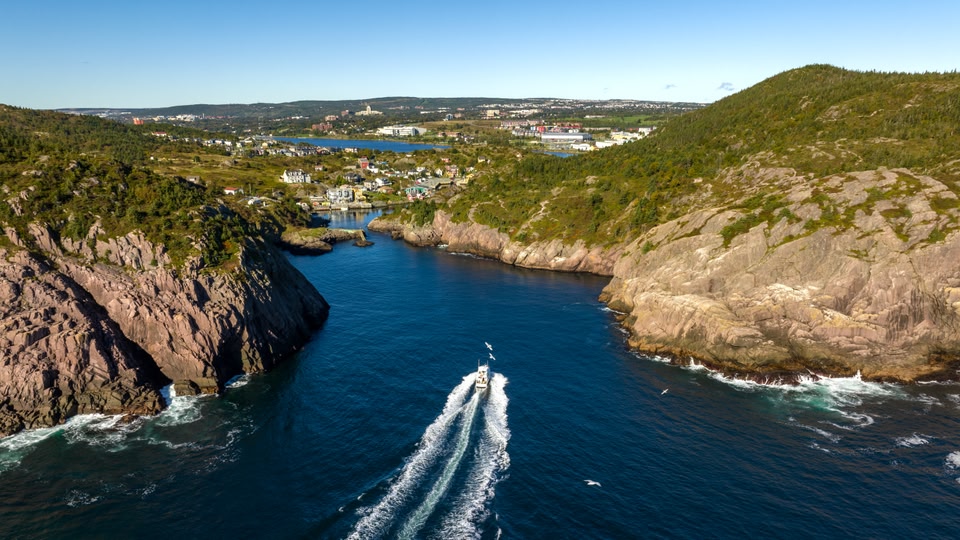Aerial view of a coastal landscape with a boat navigating through blue waters flanked by rocky cliffs and green hills.
