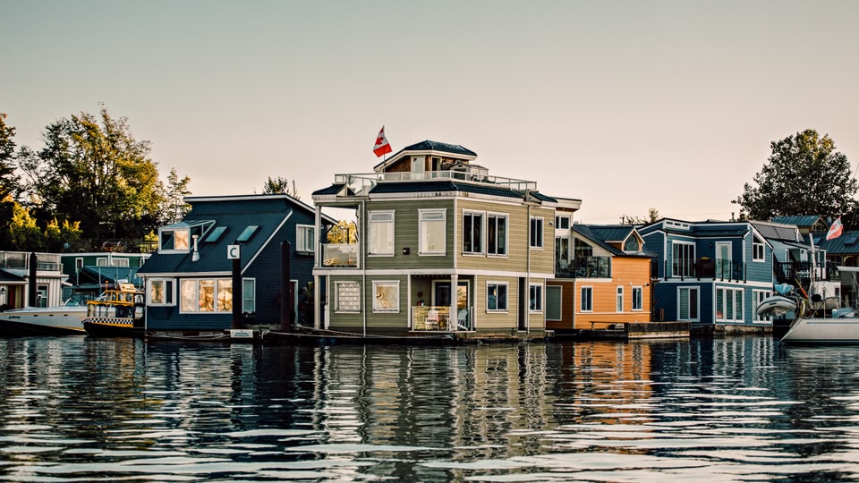 A row of colorful floating homes along a calm waterway in Victoria, British Columbia.