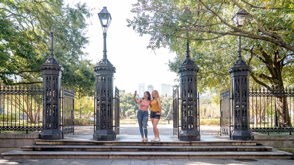 Two women standing in front of an ornate gate in a park, taking photos.