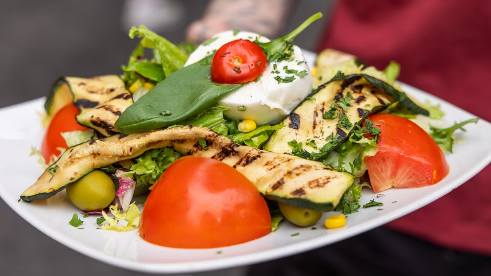 A close-up of a plate filled with a vibrant salad featuring grilled vegetables, tomatoes, and a creamy white cheese.