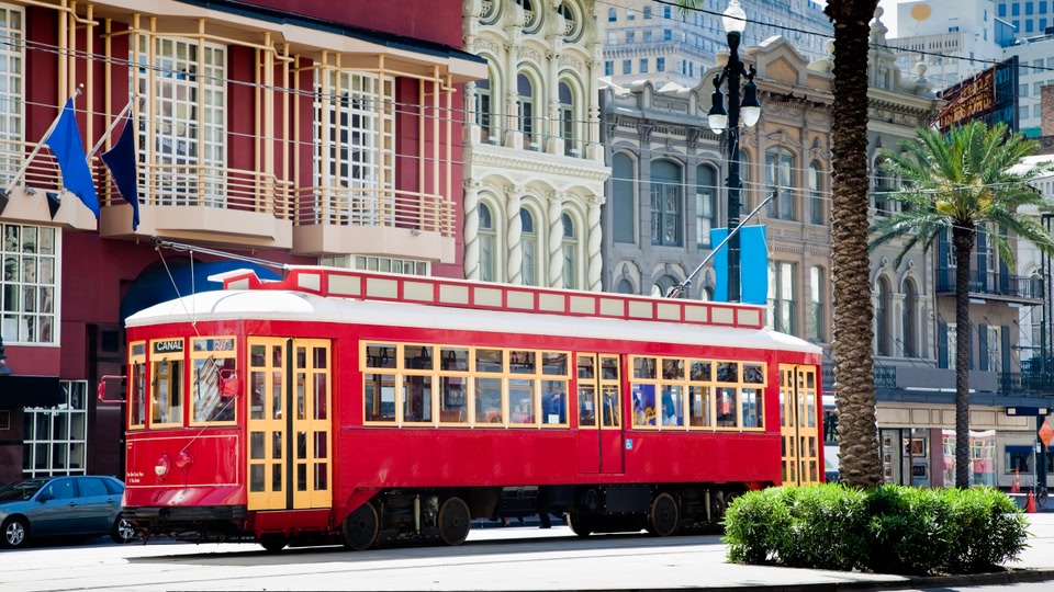 A historic red streetcar with yellow doors and trim, labeled 'CANAL', driving down a city street lined with classic architecture in New Orleans.