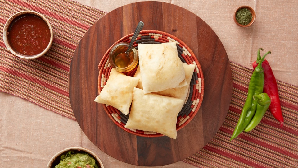 A wooden plate with several pieces of fried empanadas, accompanied by a side of sauce and a bowl of guacamole.