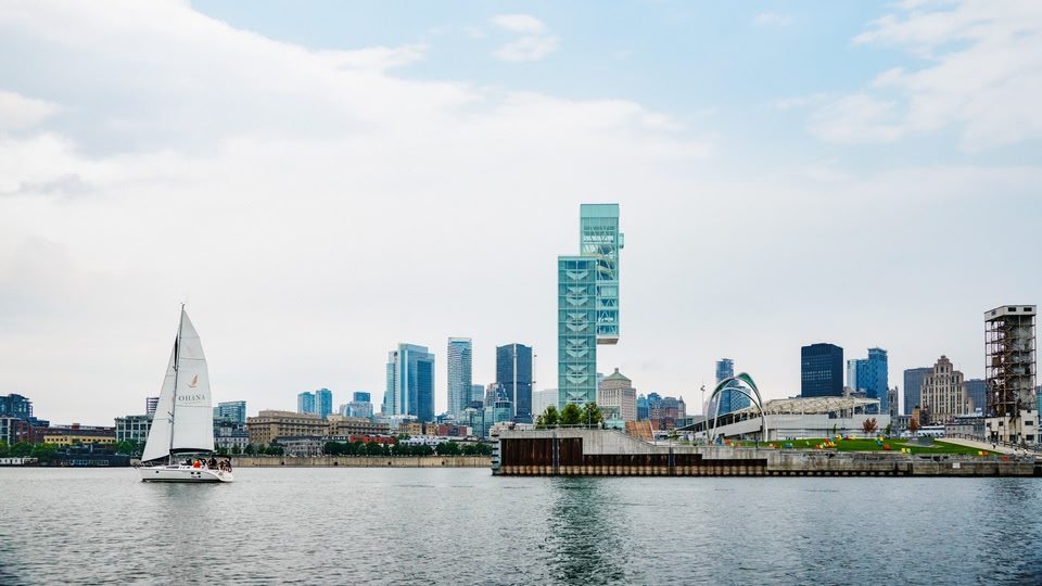 A sailboat named Ohana sails on a body of water with a modern city skyline in the background.