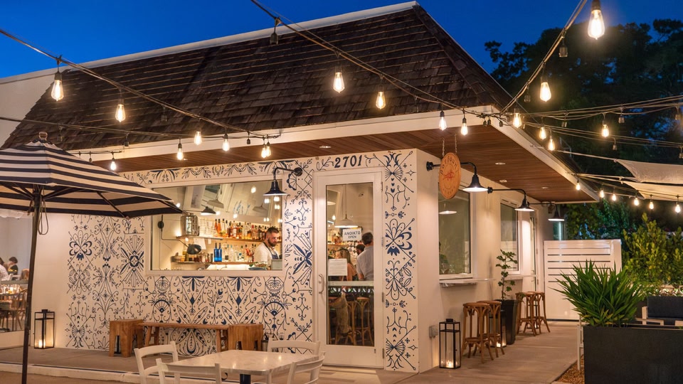 Exterior of a stylish bar at night with string lights and patrons inside.