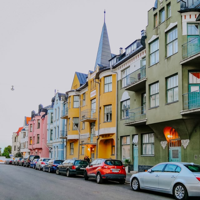 A colorful row of residential buildings in Helsinki, Finland, with parked cars in front.