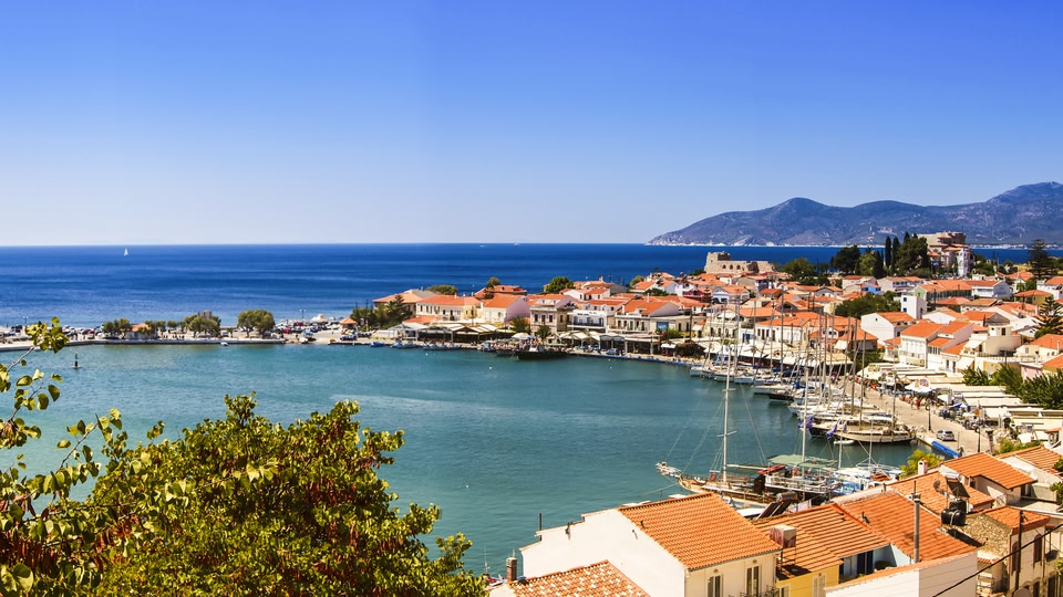 Aerial view of a coastal town with red-roofed buildings and a marina full of sailboats.