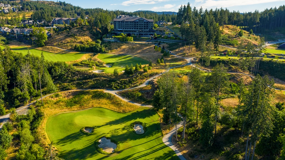 Aerial view of a golf course with green fairways, sand bunkers, and a winding path through a forested area.