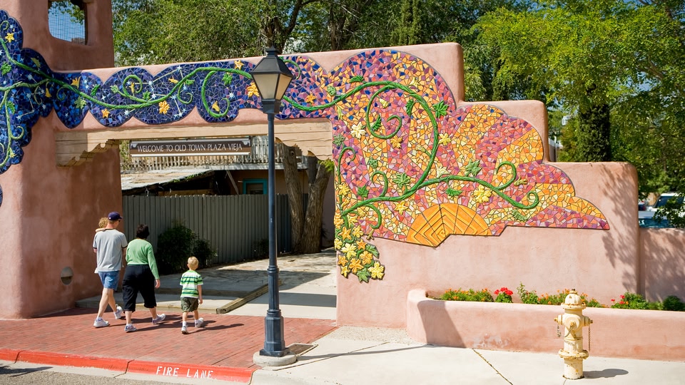 Entrance to Old Town Plaza Vieja in Albuquerque, New Mexico, with colorful mosaic archway and people walking by.