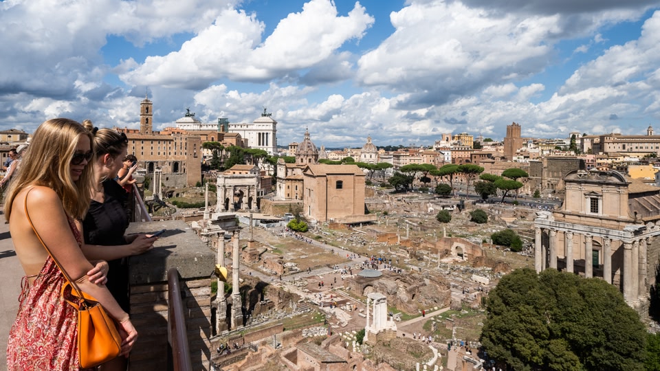 Aerial view of the Roman Forum ruins in Rome, showcasing ancient architecture and columns under a cloudy sky.