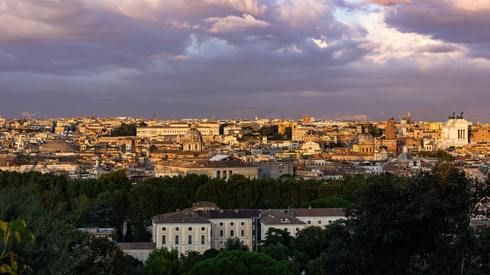 A panoramic view of Rome's skyline with various historic buildings and domes visible under a cloudy sky.