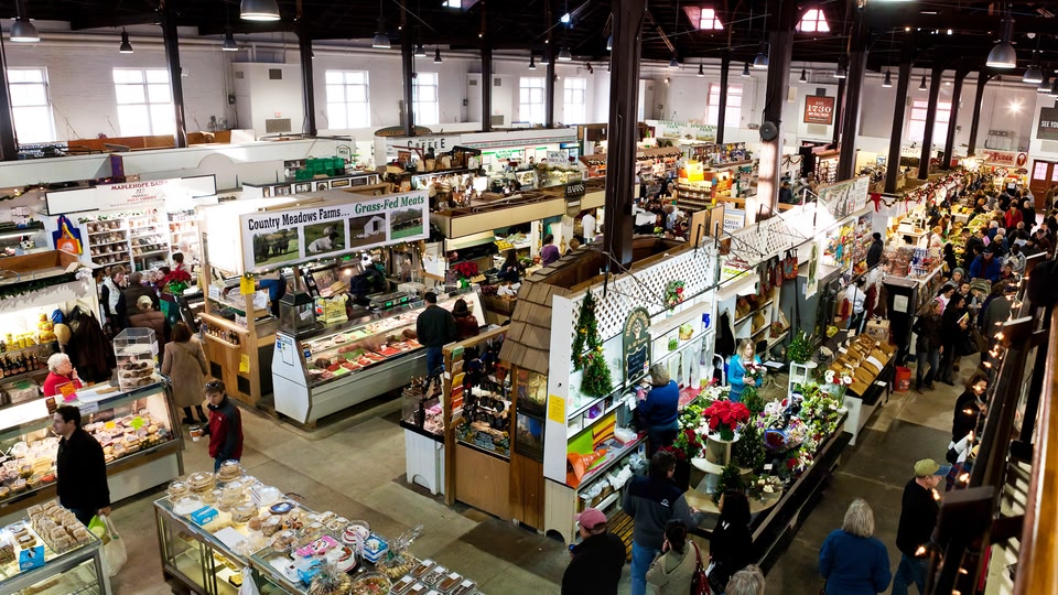 An indoor market with numerous stalls selling food and various products, bustling with shoppers.