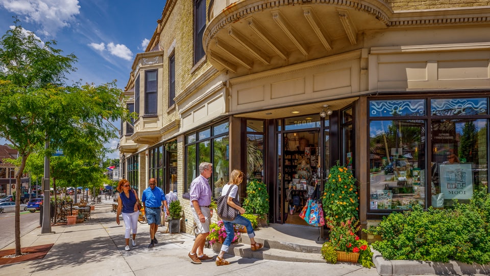Three people walking past shops on a sunny day in Milwaukee, Wisconsin.