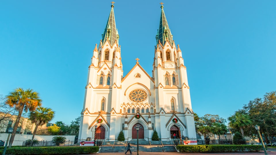 A large, ornate cathedral with two tall spires and a detailed facade, located in Savannah, Georgia.