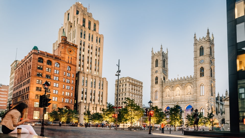 A cityscape with a woman sitting on a ledge, historic buildings, and a church in the background.