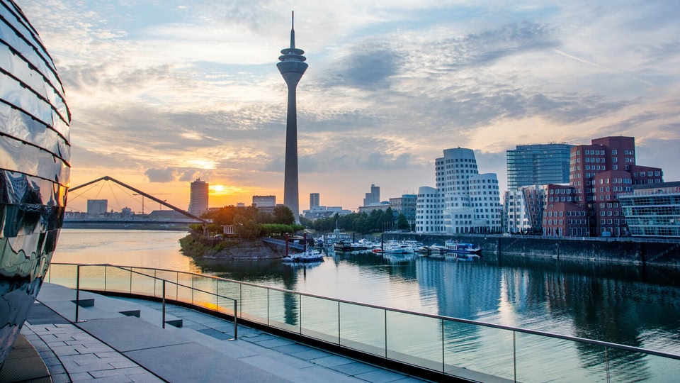 A view of the Dusseldorf skyline at sunset with the Rhine River in the foreground.