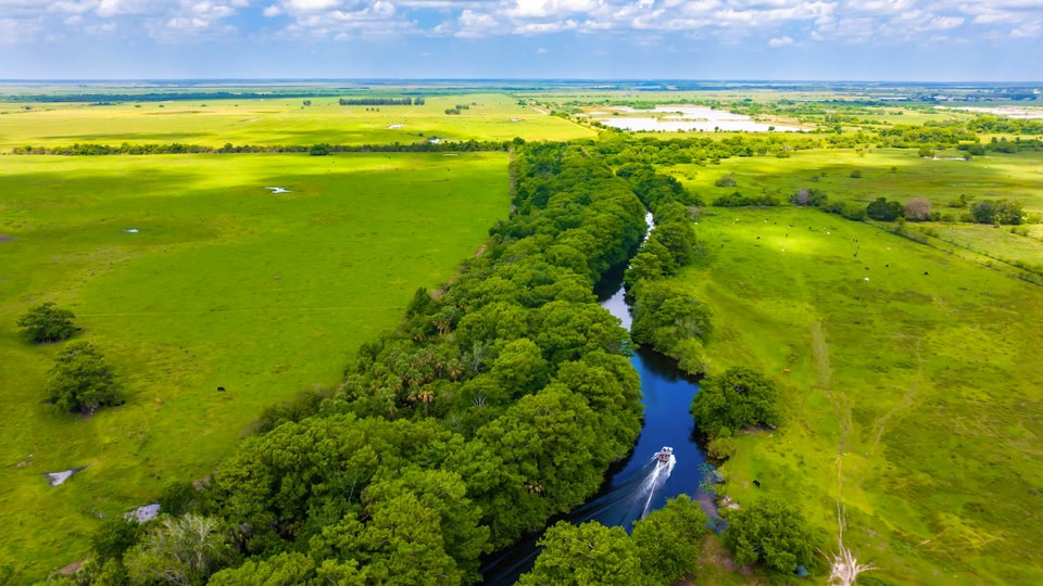 Aerial view of a river winding through a lush green landscape with a boat traveling on the water.