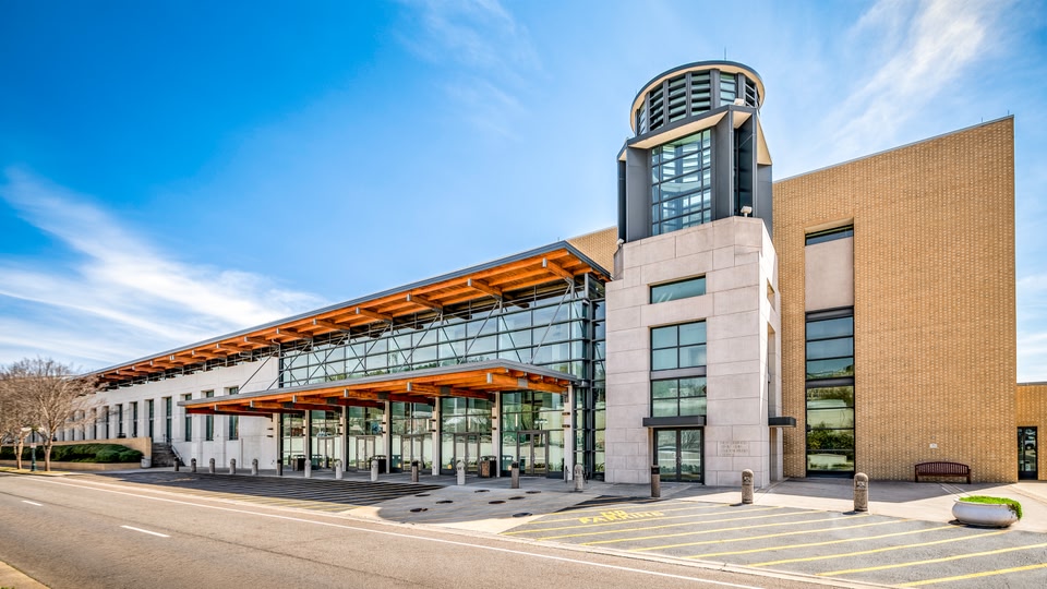 Modern hotel building with a unique tower and glass facade, located along a road with parking spaces in front.