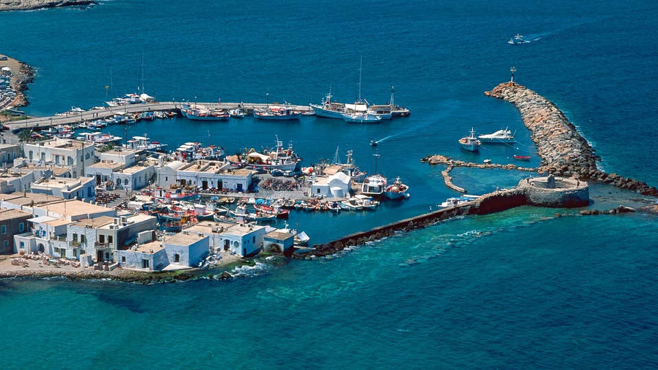 A view of the picturesque white buildings of Naoussa town in Greece, with a church in the background and the sea in the foreground.